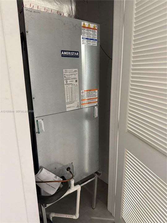 Ameristar HVAC air handler unit mounted on a metal support frame with connected PVC drain piping and louvered closet door access