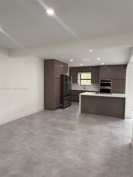 Kitchen featuring high-gloss slab cabinetry, central island with stone-surface countertop, built-in double wall oven, and large-format porcelain tile flooring