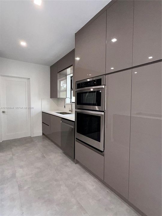 High-gloss cabinetry, built-in stainless steel double wall ovens, integrated dishwasher, solid surface countertops, and large-format tile flooring