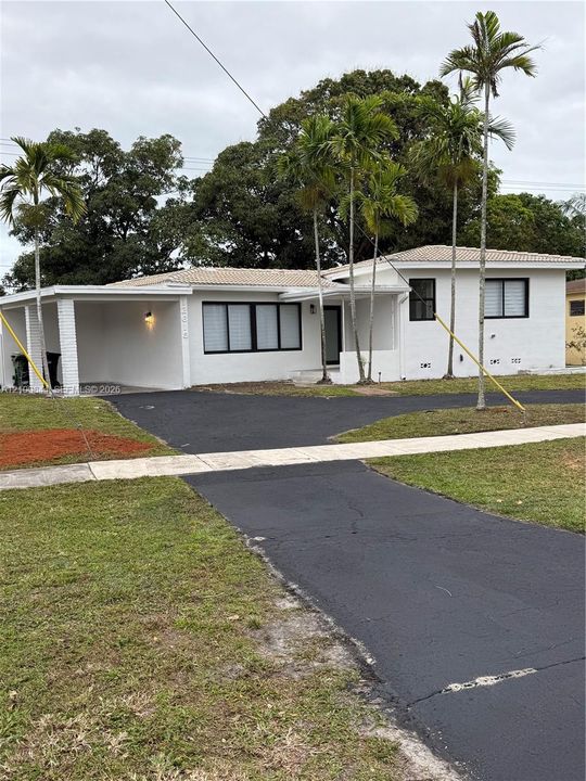 Single-story residence featuring a painted masonry exterior, a covered carport, a tile roof, and black-framed windows