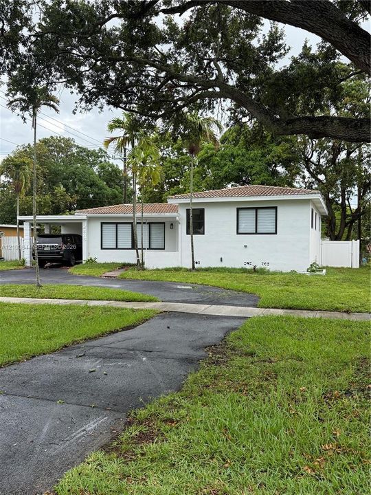 Single-story exterior featuring white masonry walls, a tile roof, an attached carport, and window frames with black trim