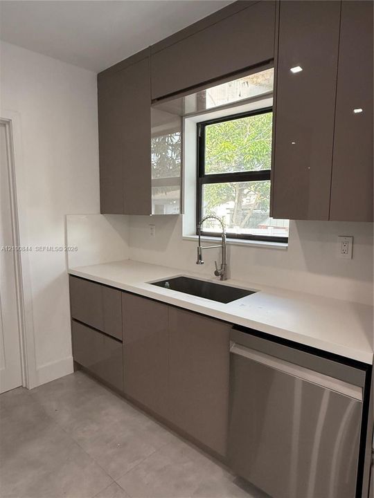 Modern kitchen featuring high-gloss cabinetry, stone-surface countertops, stainless steel undermount sink, commercial-style pull-down faucet, and neutral tile flooring