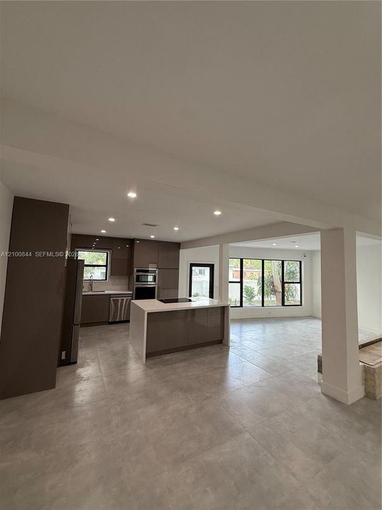 Kitchen featuring high-gloss cabinetry, stone-surfaced center island, stainless steel built-in appliances, large-format tile flooring, and recessed lighting