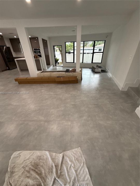 Large-format neutral tile flooring, kitchen featuring a central island with integrated cabinetry, structural support pillars, and black-framed windows
