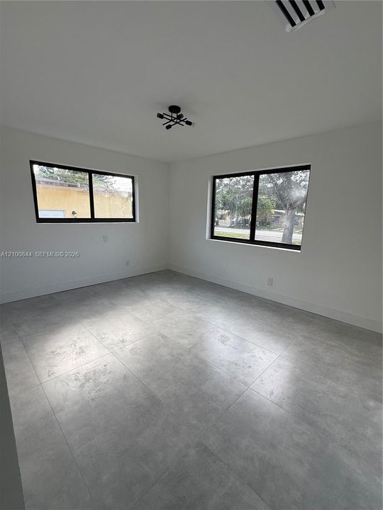 Large-format tile flooring, dual windows with dark frames, and a geometric multi-arm ceiling fixture