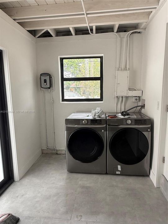 Utility area featuring concrete flooring, exposed ceiling joists, white walls, and a single-pane window