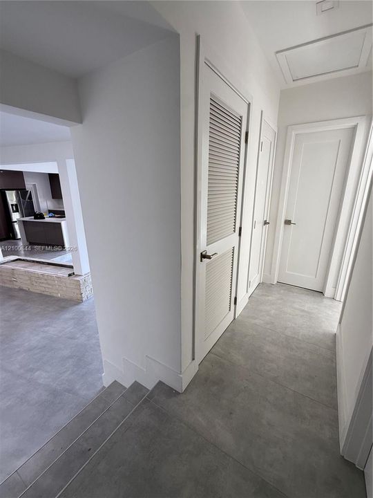 Hallway featuring large-format tile flooring, solid-core interior doors with satin nickel hardware, and a louvered utility closet door