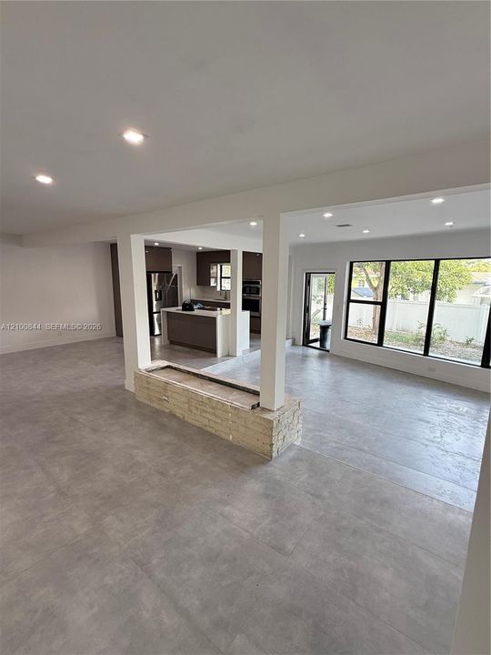 Large-format tile flooring, recessed lighting, brick-accented partition wall, kitchen island with stone-surface countertop, and expansive window wall with external door