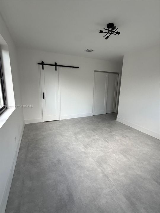 Room featuring grey stone-finish tile flooring, a white sliding barn door with matte black hardware, and a modern geometric flush-mount light fixture
