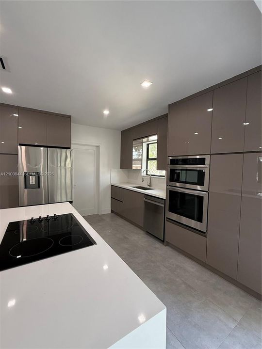 Kitchen featuring high-gloss cabinetry, a quartz countertop island with an integrated electric cooktop, stainless steel wall-mounted oven and microwave, and large-format tile flooring