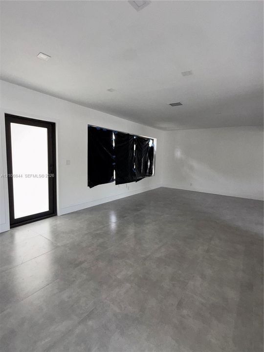 Open-concept interior featuring large-format tile flooring, neutral wall finishes, recessed ceiling lighting, and a multi-pane glass-panel exterior door