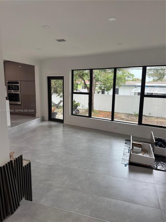 Large-format grey tile flooring, floor-to-ceiling multi-panel windows with black frames, built-in dual wall ovens, flat-panel cabinetry, and recessed ceiling lighting