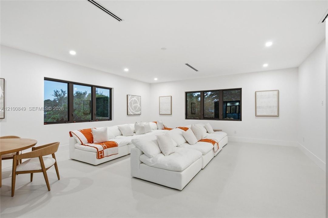 Open-concept interior featuring smooth white flooring, recessed ceiling lighting, linear ceiling vents, and large-format windows with dark frames