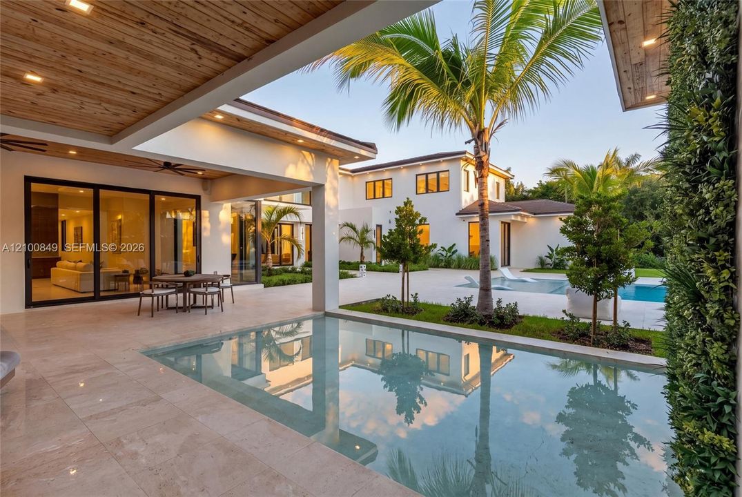 Covered outdoor patio with a natural wood-finish ceiling, stone tile flooring, built-in recessed lighting, integrated swimming pool, and landscaping