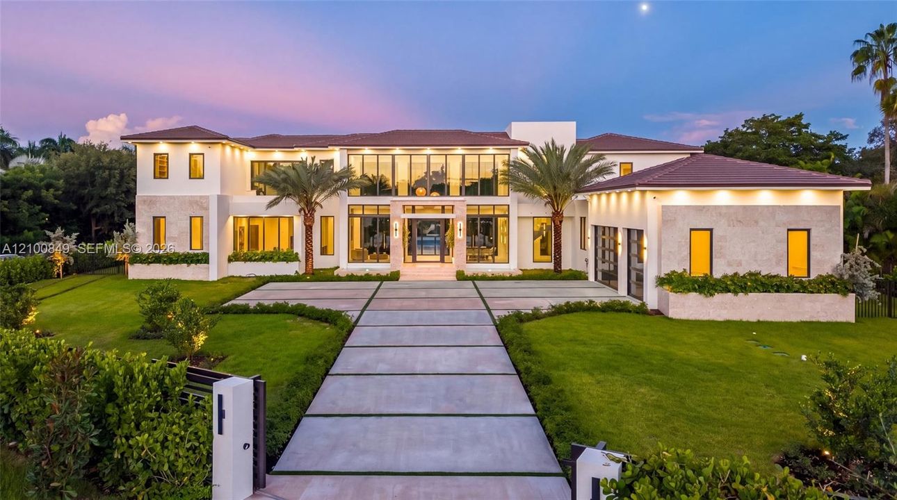 Contemporary residence featuring multi-level stone facade, floor-to-ceiling windows, tiled roof, linear paved driveway, and manicured landscaping