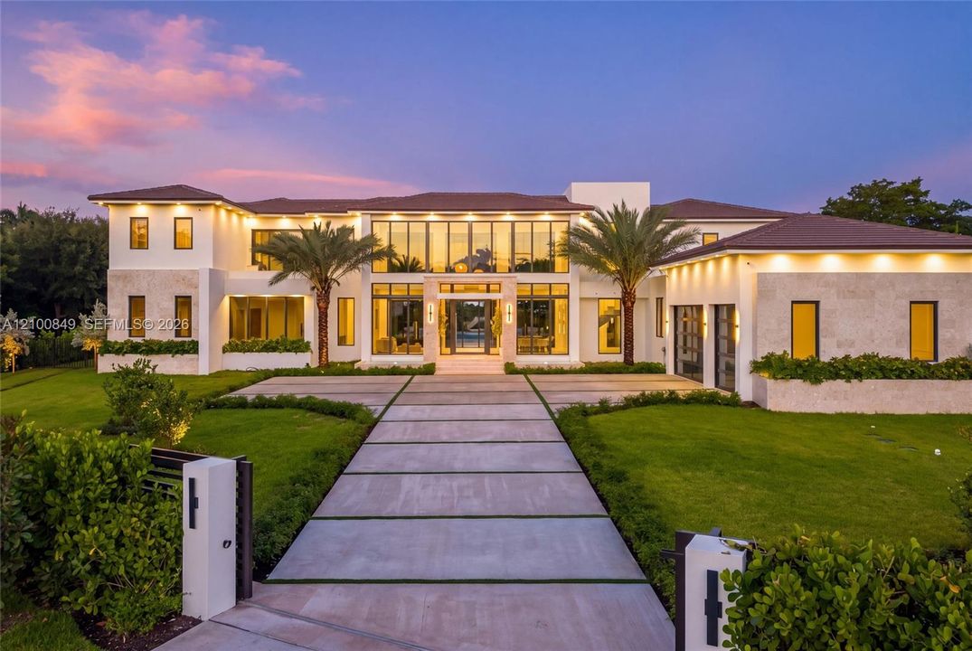 Two-story modern residence featuring stone-clad exterior walls, expansive floor-to-ceiling glass windows, a structured concrete paver driveway, and professional landscaping