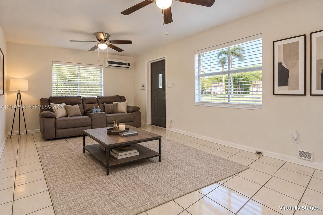 Living area featuring tile flooring, dual ceiling fans, wall-mounted air conditioning unit, and windows fitted with horizontal blinds