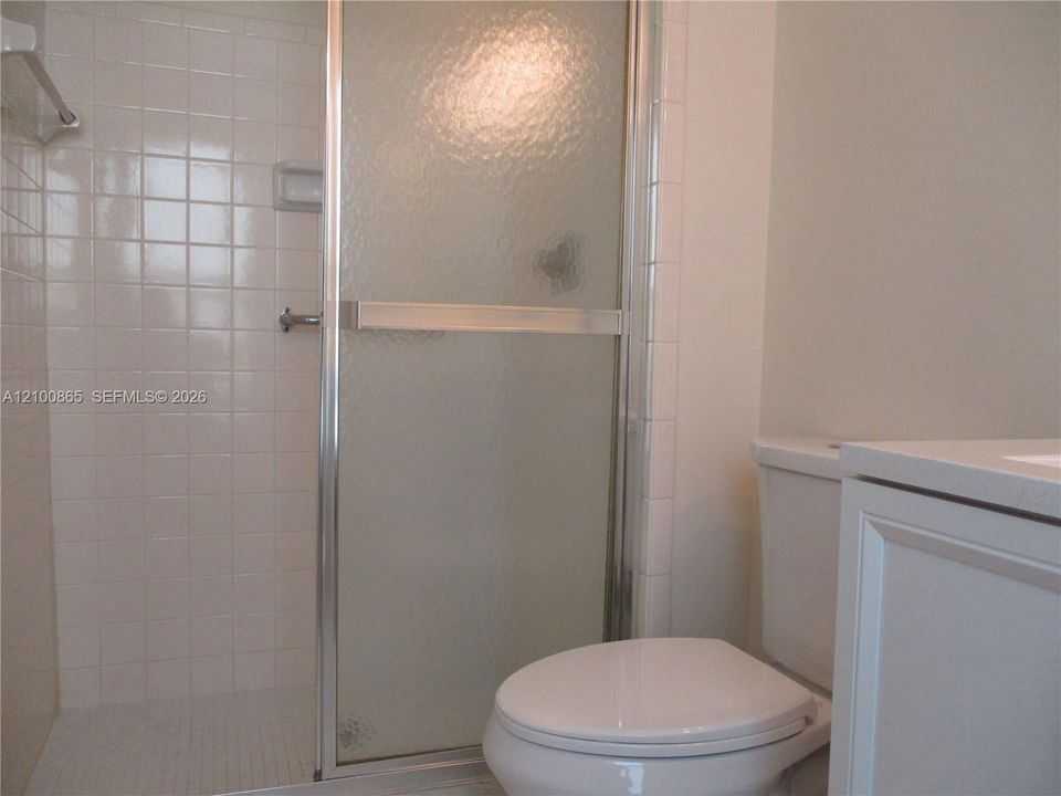 Master bathroom Shower stall with white square wall tile, semi-frameless textured glass door, and built-in soap niche, paired with a white vanity and porcelain commode
