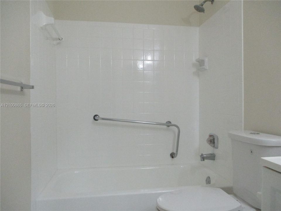 Guest Bathtub enclosure featuring white ceramic wall tiles, a built-in soap dish, a wall-mounted metal grab bar, and a standard metal shower head and faucet fixture