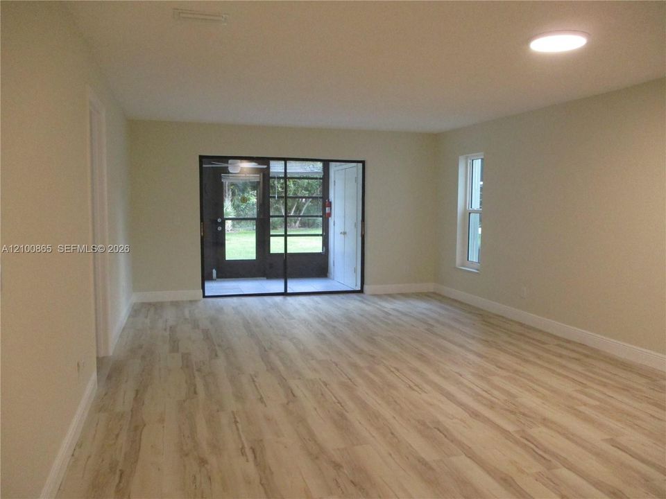 Open-concept interior featuring light wood-finish flooring, recessed lighting, and large sliding glass doors with a black frame leading to a screened enclosure