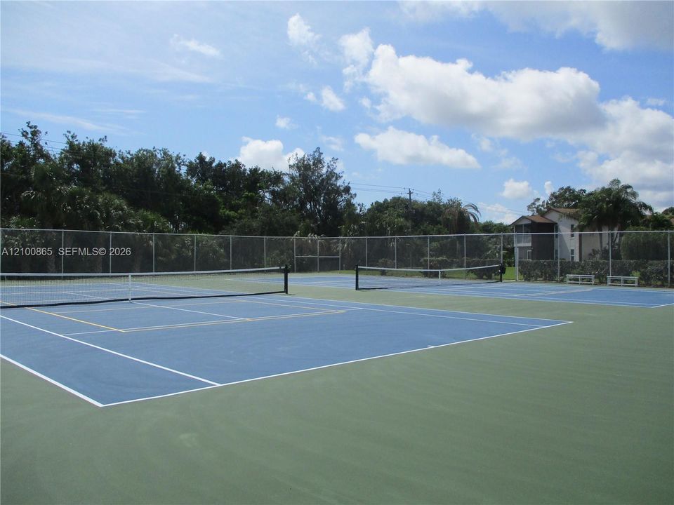 Dual hard-court tennis/pickle ball facility featuring blue and green surfacing, white court markings, central nets, and full-perimeter chain-link fencing
