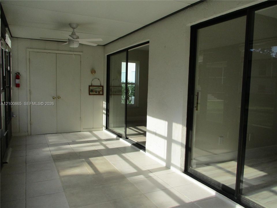Tiled flooring with large format tiles, sliding glass doors with black frames, white ceiling fan, and built-in closet with bifold doors. Slidering door into the living area and master bedroom