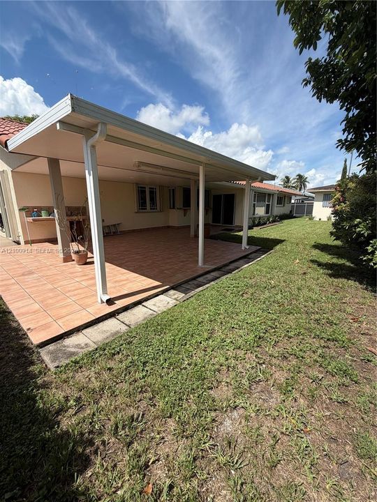 Covered rear patio featuring terracotta-style tile flooring, a built-in outdoor prep counter, and a light-colored stucco exterior