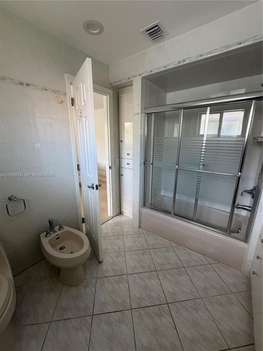 Bathroom featuring tile flooring, full-height wall tiling, a built-in floor-to-ceiling storage cabinet, and a bathtub with a sliding glass enclosure