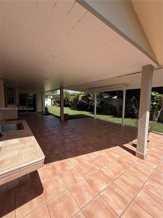 Exterior side yard featuring a concrete walkway, tiled patio area, and white metal security window grilles