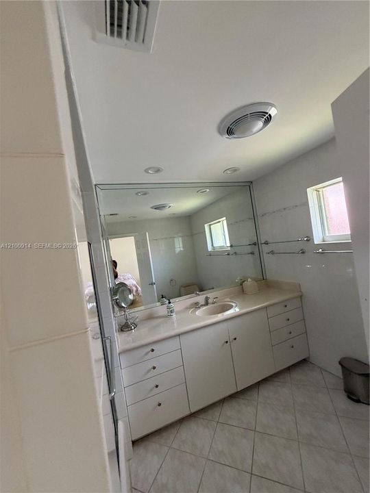 Bathroom featuring a solid-surface vanity with an integrated sink, expansive wall-to-wall mirror, neutral tile flooring, and metallic wall-mounted towel bars