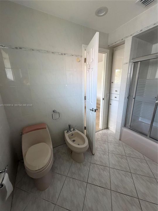 Bathroom featuring neutral tile wall wainscoting with decorative accent trim, floor-to-ceiling built-in cabinetry, and a shower-tub combination with a metal-framed glass enclosure
