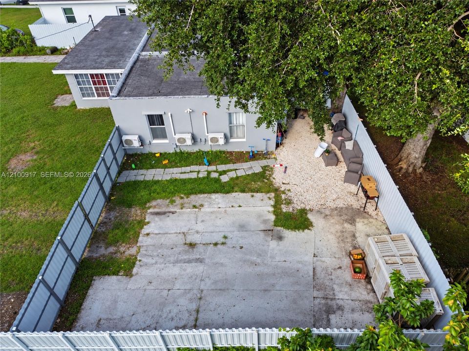 Fenced outdoor space featuring a paved area, gravel section, and mature trees