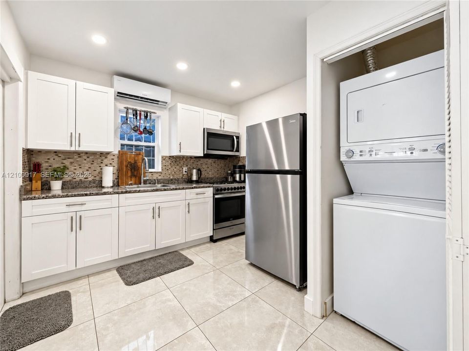 Kitchen featuring white cabinetry, stainless steel appliances, granite-style countertops, and a mosaic tile backsplash