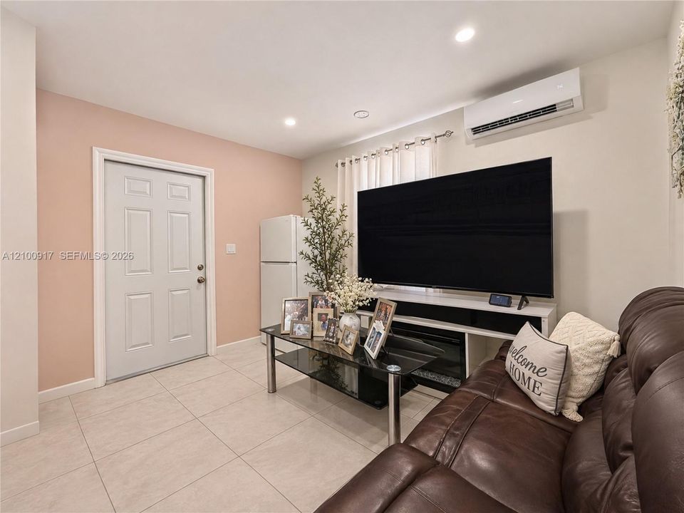 Recessed ceiling lighting, wall-mounted air conditioning unit, white paneled door, and light-toned tile flooring