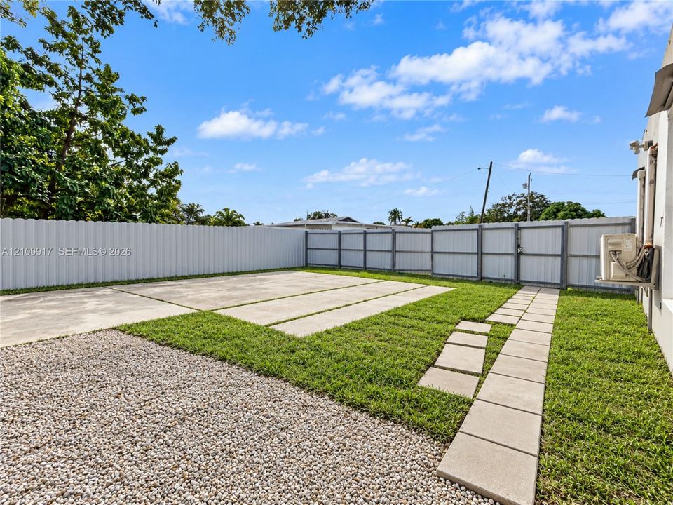 Expansive outdoor space featuring a gravel and concrete pad, a concrete paver walkway, and a perimeter fence