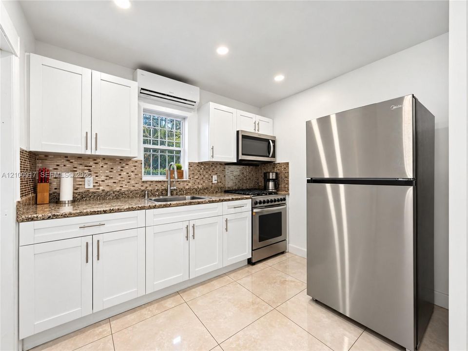 Kitchen featuring stainless steel appliances, granite countertops, white cabinetry, a tiled backsplash, and recessed lighting