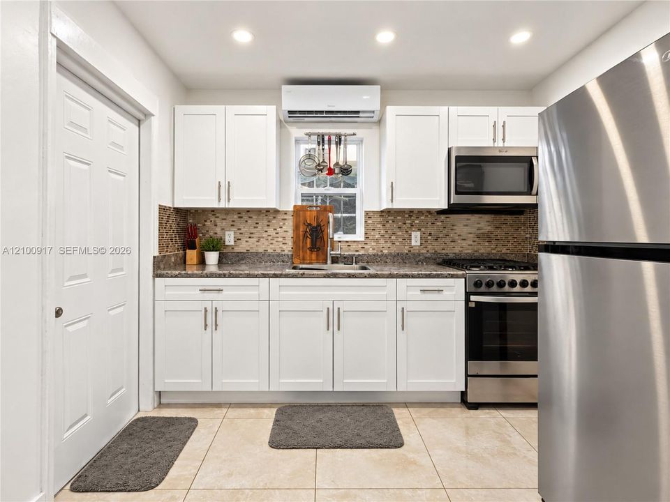 Kitchen featuring white cabinetry, granite countertops, stainless steel appliances, mosaic tile backsplash, and recessed lighting