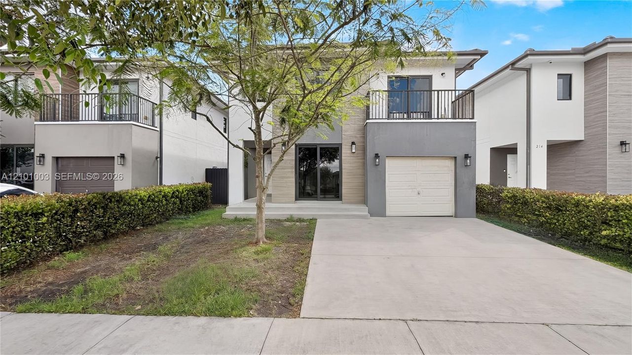 Two-story contemporary exterior featuring mixed-texture siding, a paved concrete driveway, a private second-story balcony with metal railings, and a single-car garage