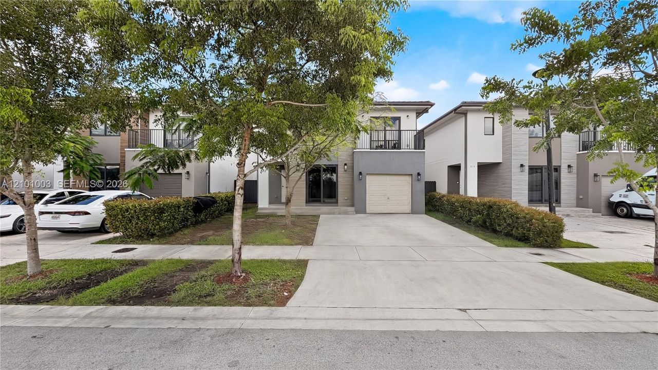 Multi-story exterior featuring a concrete driveway, attached garage, private second-story balcony with metal railings, and a landscaped hedge border