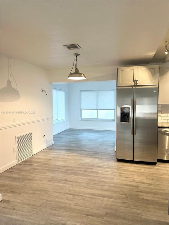 Kitchen featuring wood-finish flooring, stainless steel refrigerator, white shaker-style cabinetry, and pendant lighting