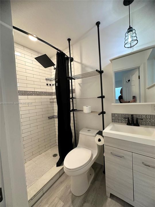 Bathroom featuring a white subway tile shower surround with decorative accent inlay, a square rain-style showerhead, wood-finish cabinetry with a white basin, matte black faucet hardware, and wood-finish flooring