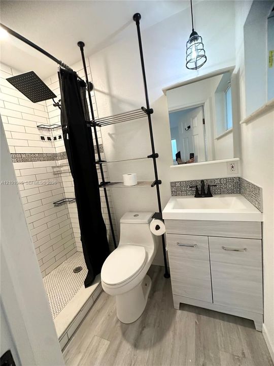 Bathroom featuring wood-finish cabinetry, a rectangular sink with a matte black faucet, a shower with white subway tile walls and decorative tile accents, a hexagonal tile shower floor, and matte black rainfall showerhead