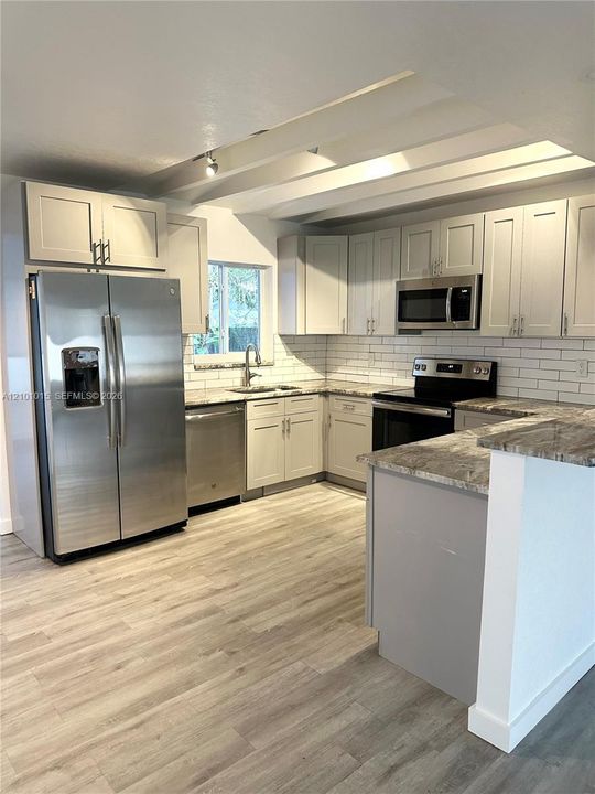 Kitchen featuring white cabinetry, stone-finish countertops, subway tile backsplash, stainless steel appliances, and wood-finish flooring