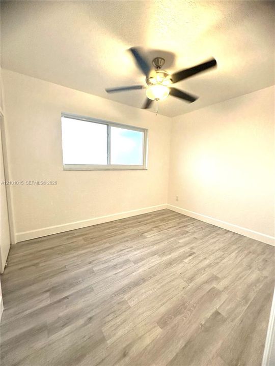 Neutral-toned interior room featuring wood-finish flooring, a horizontal sliding window, and a central ceiling fan with integrated lighting