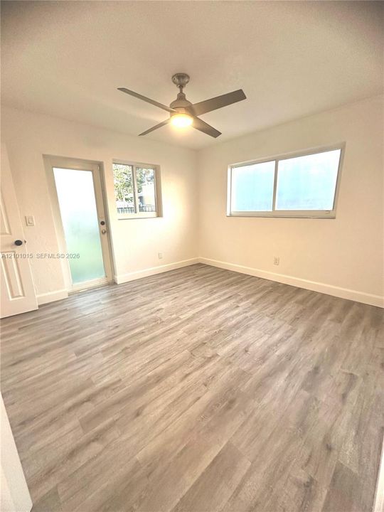 Room featuring wood-finish flooring, a ceiling fan with integrated lighting, dual-pane horizontal sliding windows, and a glass-paneled exterior door