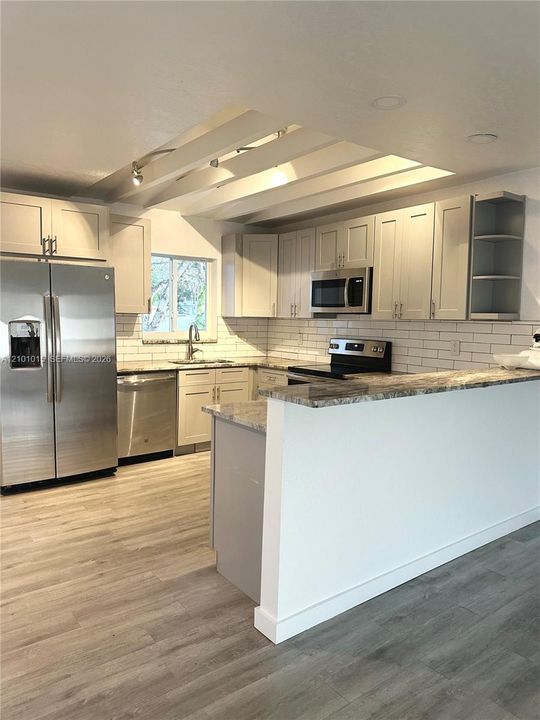 Kitchen featuring shaker-style cabinetry, stone countertops, stainless steel appliances, subway tile backsplash, and recessed ceiling lighting
