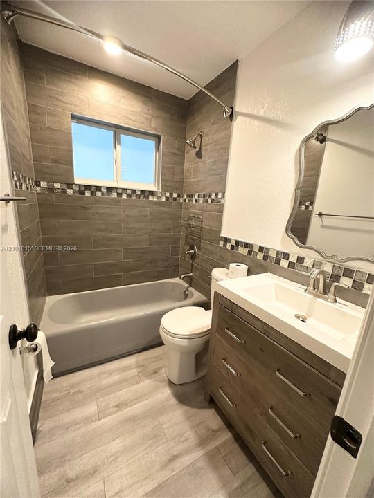 Bathroom featuring a vanity with a white rectangular integrated sink, wood-finish cabinetry, tile wall surround with decorative mosaic accent, and wood-finish flooring