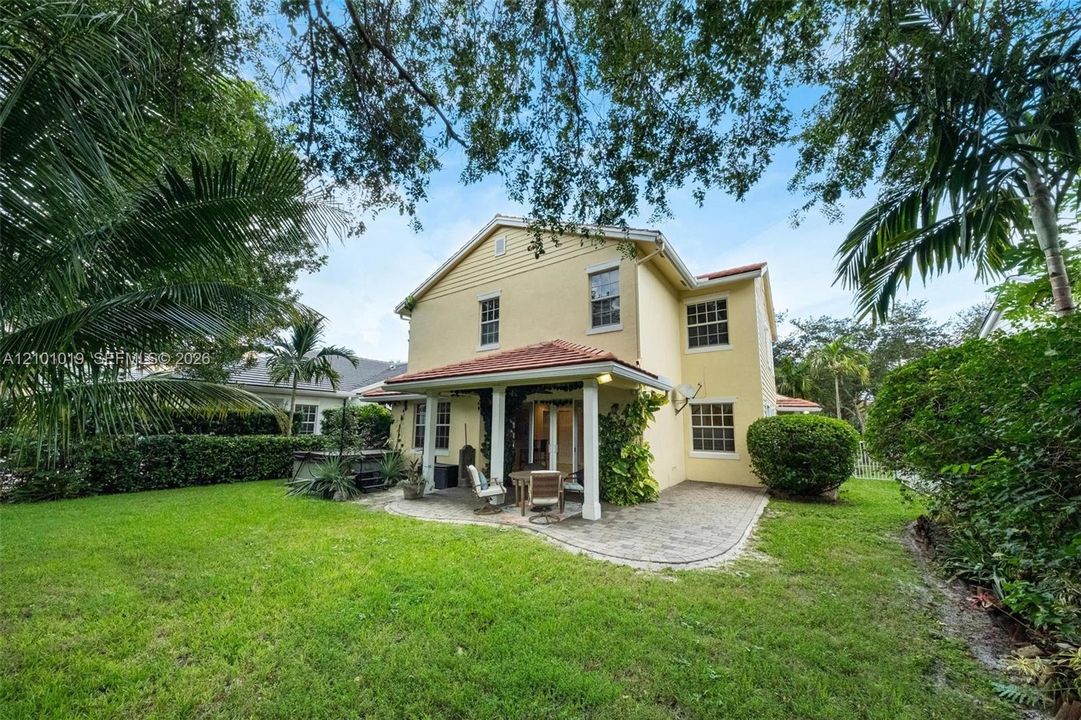 Stucco exterior featuring a covered patio with concrete pavers, a tile roof, mature landscaping, and an expansive lawn