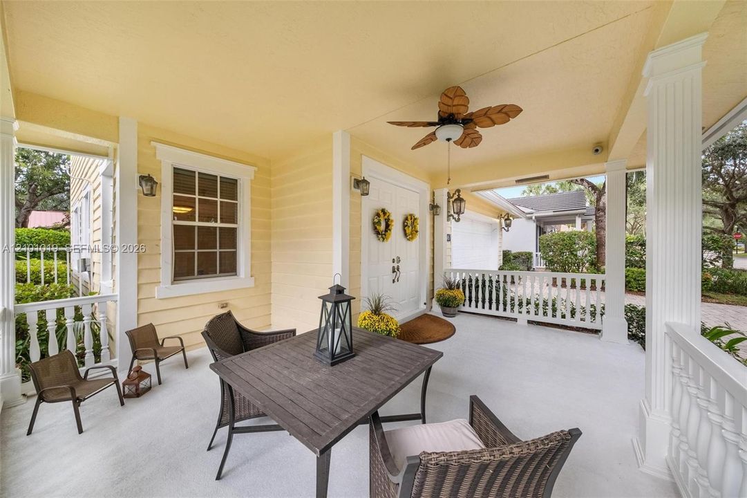 Covered front porch featuring white railings, structural columns, a ceiling-mounted fan, and double-entry doors