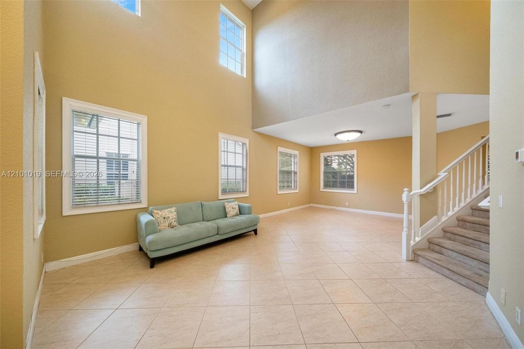 Expansive living area featuring vaulted ceilings, oversized windows for natural light, ceramic tile flooring, and a staircase with white balusters